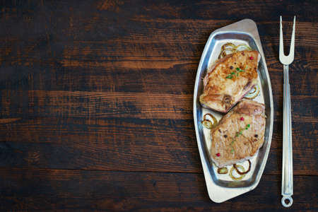 Roasted meat on a metal plate and fork. Top view with copy space.