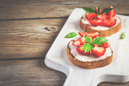 Summer breakfast bruschetta with strawberries, basil and cottage cheese. Top view with copy space, tintedの写真素材