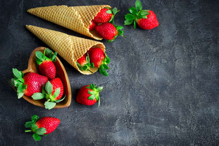 Waffle cone with ripe strawberries. Berry composition on a dark background. Top view with copy spaceの写真素材