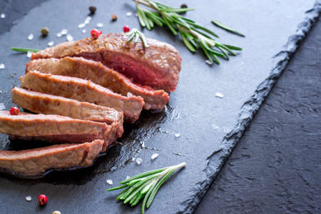 Roast beef steak with rosemary on slate cutting board. Grilled meat closeup, selective focusの写真素材