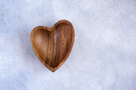 Wooden bowl in the shape of heart on a concrete background.
