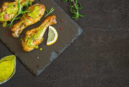 Roasted chicken drumstick In green sauce with lemon on a black background. Top view with copy spaceの写真素材