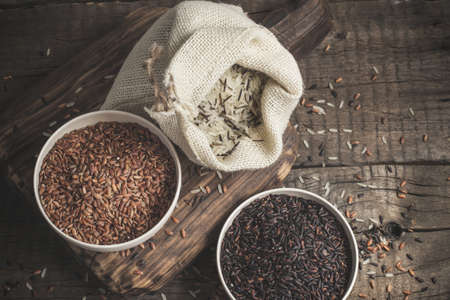 Selection of red, black and mixed rice on an old wooden background.Top view with copy spaceの写真素材