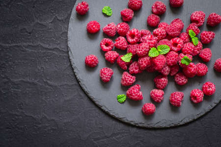 Ripe raspberries on slate dish on black background.