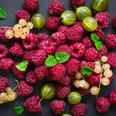 scattering of delicious berries on a black background. Raspberries, currants and gooseberries are decorated with mint leavesの写真素材