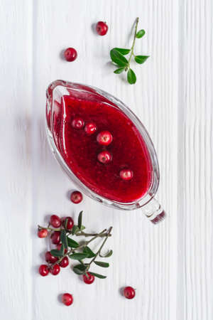 Fresh Lingonberry sauce in a gravy boat on a white wooden background.の写真素材