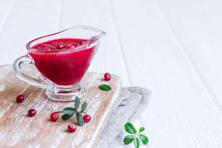 Fresh Lingonberry sauce in a gravy boat on a white wooden background.の写真素材