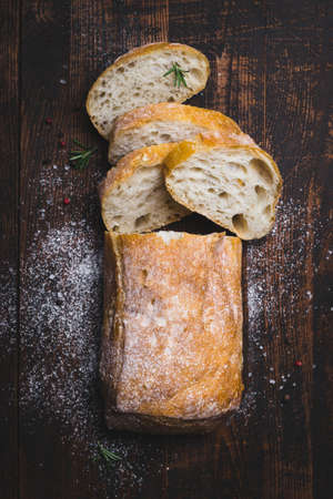 Italian ciabatta bread cut in slices on dark wooden background.の写真素材