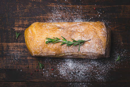 Italian ciabatta bread with branch of rosemary on dark wooden background.の写真素材