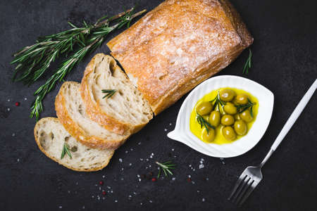 Italian ciabatta bread cut in slices with herbs and olives on black background.の写真素材