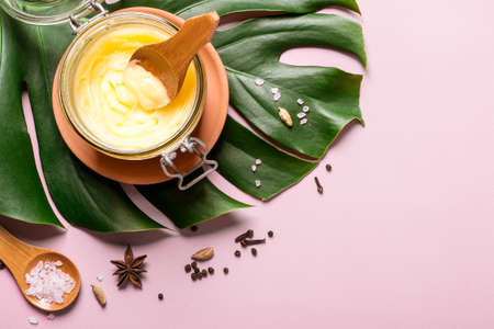 ghee butter in a glass jar, pink salt and spices on pink background.