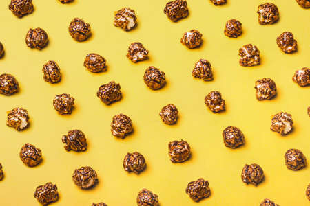 Food pattern of chocolate popcorn on a yellow background.