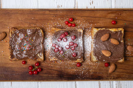 Fried toasts with chocolate cream, nuts and berries on a wooden cutting boardの写真素材