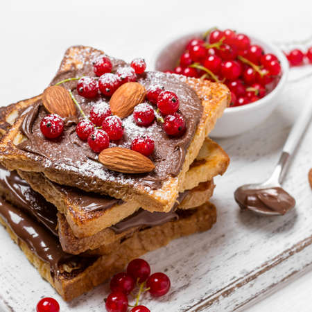 stack of fried toast with chocolate cream, red currant and almonds on a white wooden backgroundの写真素材
