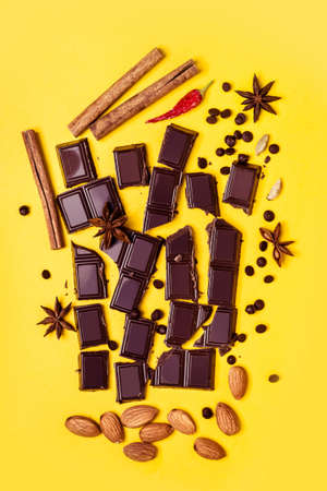 Pieces of chocolate, cinnamon, spices and almonds on a yellow background.