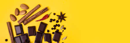 Pieces of chocolate, cinnamon, spices and almonds on a yellow background. Banner formatの写真素材
