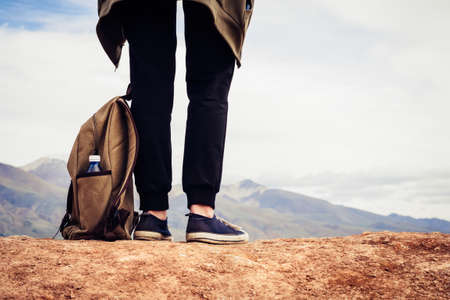 Girl tourist in black sports pants and sneakers stands on a hill. Legs of a traveler and a backpack with a bottle of water close-up.の写真素材