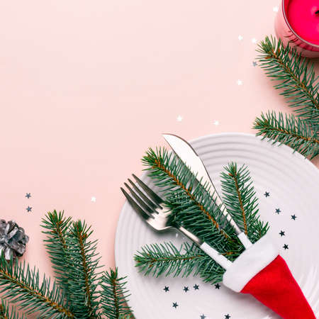 Fir branches and cutlery in Santa hat on pink background. Christmas table setting.の写真素材