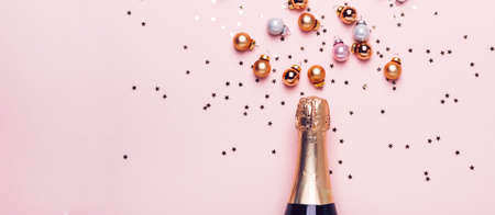 Champagne bottle and scattering of golden shiny balls and confetti on pink background, banner format.の写真素材
