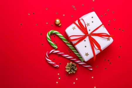 Christmas gift box and candy cane on red background.