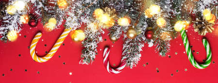 Christmas coniferous border with shining lights and candy canes on red background.の写真素材