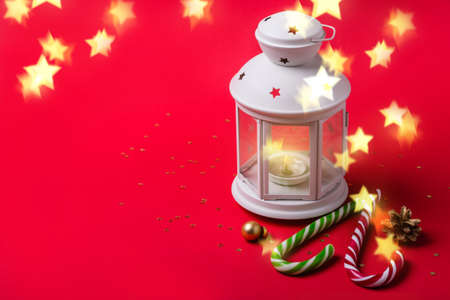 Christmas greeting card. White lantern, candy canes and glowing stars on red background.