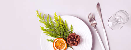 Christmas table setting. Plate and cutlery decorated with coniferous twig and dry orange. Banner...
