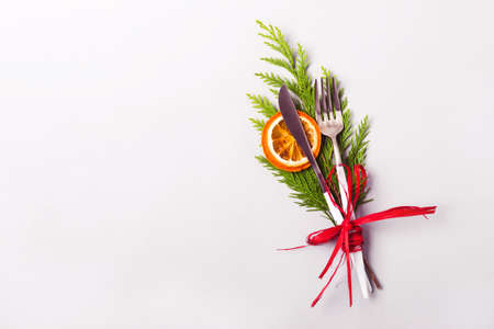 Christmas table setting concept. Fork and knife decorated with coniferous twig, dry orange and red ribbon.の写真素材