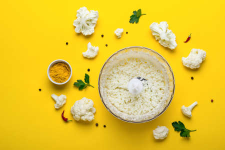 Blender bowl with freshly prepared cauliflower rice and spices on yellowの写真素材