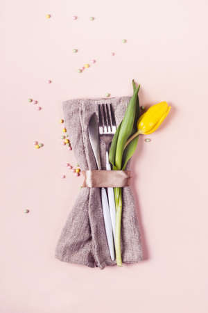 Cutlery is decorated with beautiful yellow tulip on pastel pink background. Spring Easter table setting.の写真素材