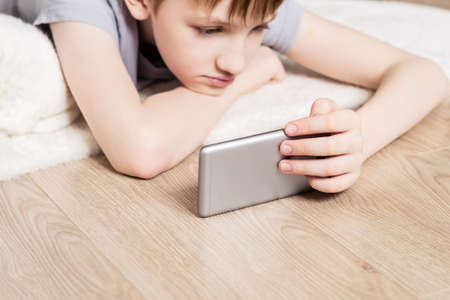 Teen boy lies on floor and watches video in smartphone. Selective focus on smartphone.