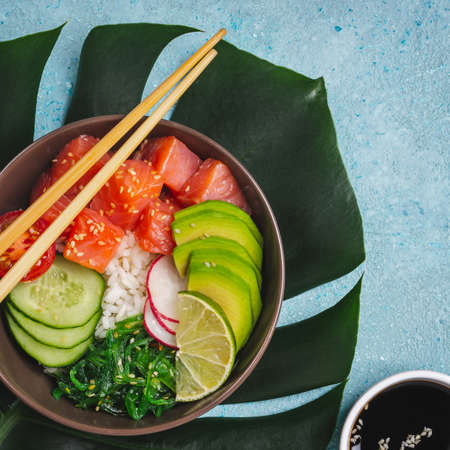Hawaiian salmon poke salad served in bowl on blue background with tropical leaves.