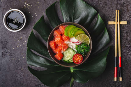 Hawaiian salmon poke salad with rice, avocado and seaweed served in bowl on tropical leaves.の写真素材