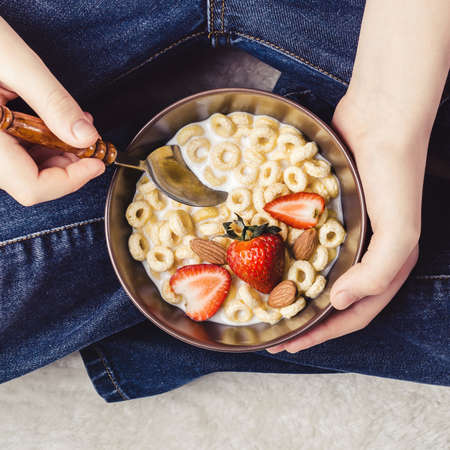 Traditional breakfast bowl. Cereal rings, strawberries and milk in bowl in teen hands.