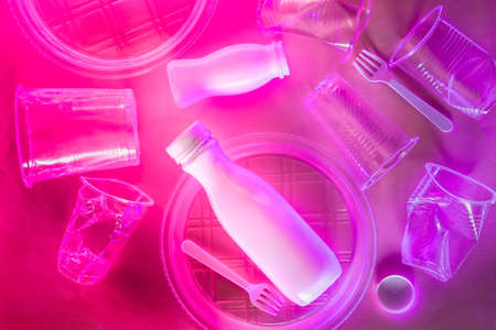 Plastic disposable tableware in red purple neon lighting. Ecology problem concept.の写真素材