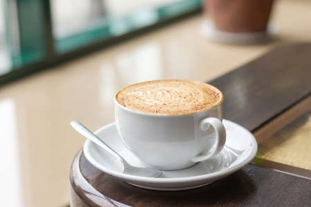 White Cup of Cappuccino with latte art. Coffee on wooden table next to cafe window.の写真素材