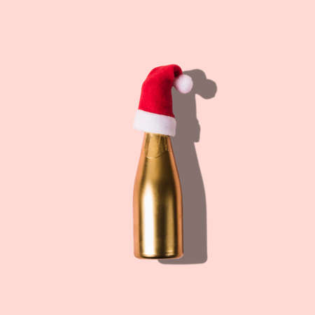 Golden champagne in Santa hat on pink background. Minimal Christmas concept.の写真素材