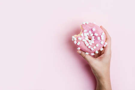 Female hand holding pink bitten donut over pinkの写真素材
