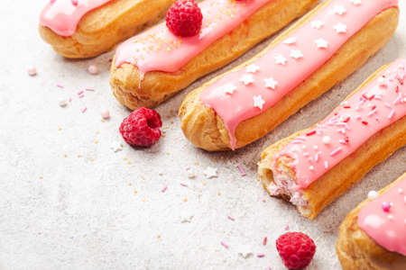 Delicious pink glazed eclairs with cream, raspberry and sugar sprinkles on gray background, copy space.の写真素材