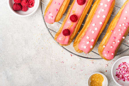Delicious eclairs with pink glaze, raspberry and sugar sprinkles on gray background.の写真素材