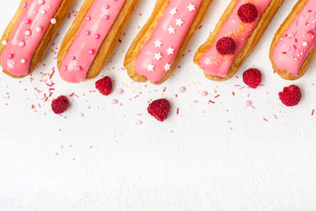 Set of delicious eclairs with pink glaze, raspberry and sugar sprinkles on white background.の写真素材