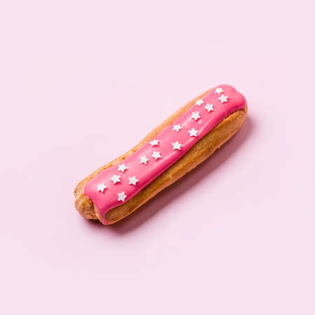 Eclair with pink icing and stars sprinkled on pink background. Food concept.の写真素材