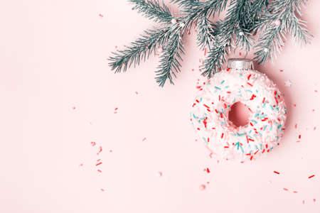 Christmas toy glazed donut with sugar sprinkling hanging on Christmas tree branch. Pink pastel background.の写真素材