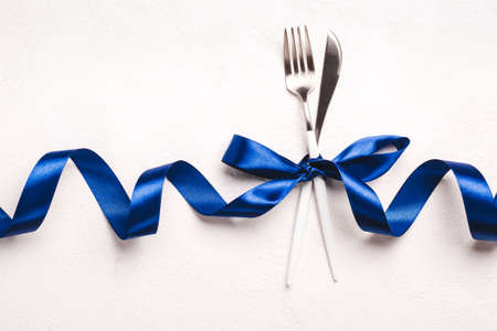 Christmas cutlery set with classic blue ribbon on white stone background.の写真素材