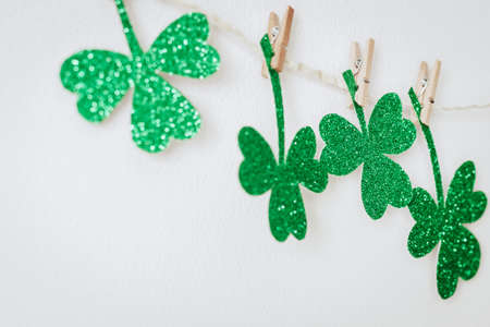 Green glitter shamrocks decoration. Homemade garland of rope and clover leaves on clothespins