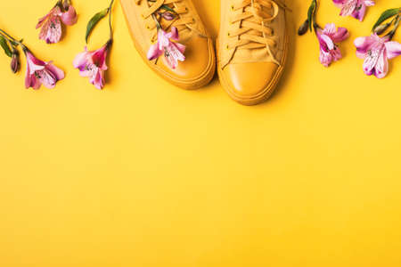 Pair of yellow sneakers and flower buds on a yellow background. Spring summer fashion concept.の写真素材