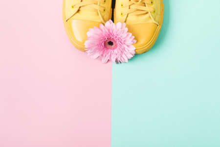 Yellow sneakers and pink flower on paper background. Spring summer fashion concept, delicate pastel colors.の写真素材