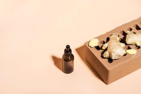 Organic Ginger essential oil in dark glass bottle, ginger root and brick on beige background. Isometric view, copy space.の写真素材