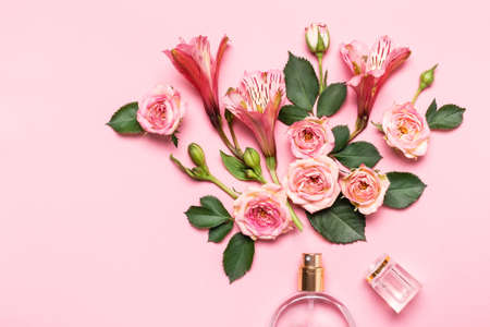 Bottle of perfume and flower arrangement of rosebuds on pink background.