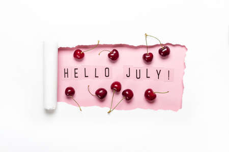 Hello July text and paper hole with cherries on pink background. Hello July conceptの写真素材